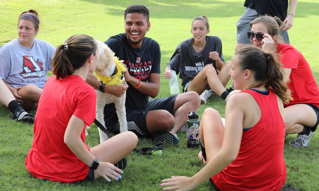 A group of students sits on the bright green grass laughing and smiling